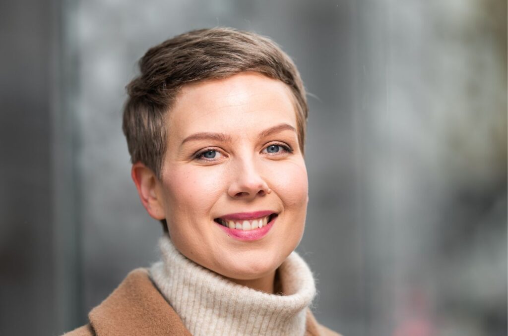 Vihreiden kansanedustaja Jenni Pitko katsoo suoraan kameraan taustallaan rauhallinen kaupunkimiljöö.